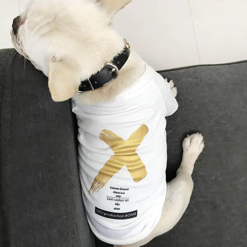 French bulldog wearing white pet shirt with gold X design, cozy on gray couch