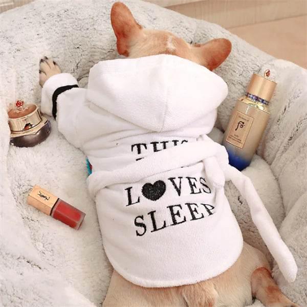 Cute dog in white 'This Loves Sleep' hoodie, relaxing in cozy pet bed with beauty products nearby