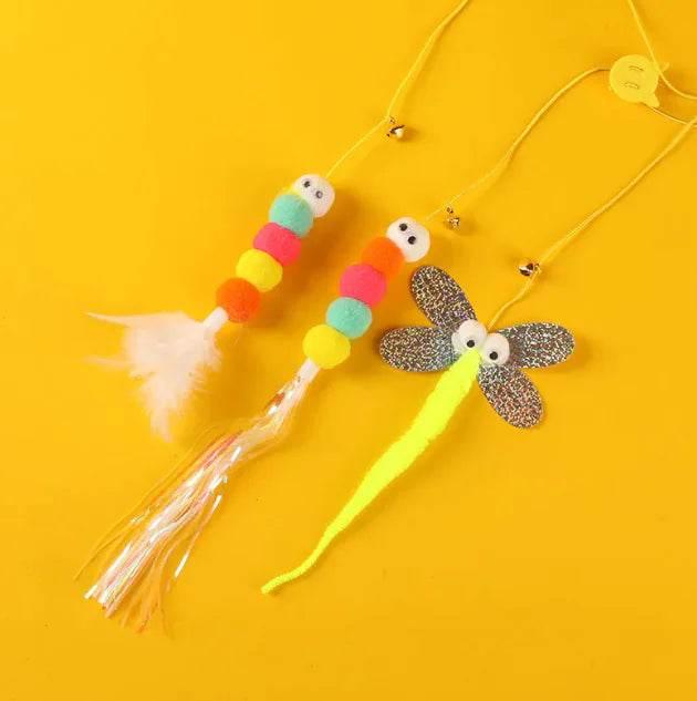 Colorful cat toys with pom poms, feathers, and dragonfly design on yellow background