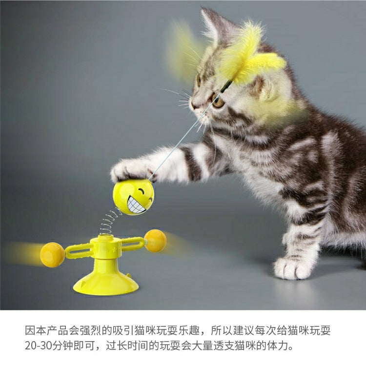 Playful tabby kitten batting at yellow smiley face cat toy with feather wand, fun pet accessory for indoor play.