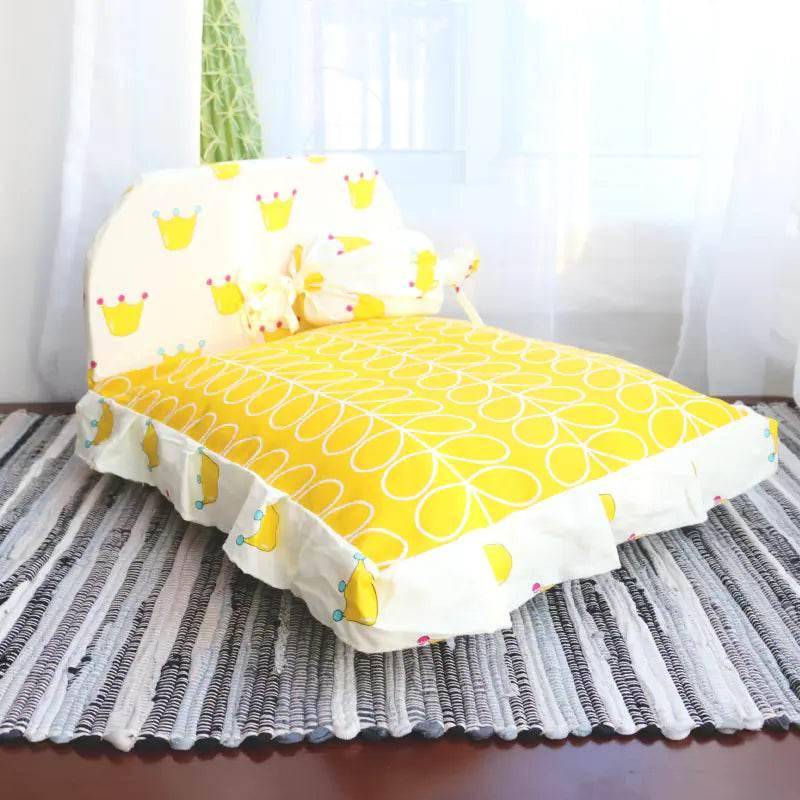 Yellow crown-patterned pet bed with ruffled edges, cozy dog or cat bedding on striped rug