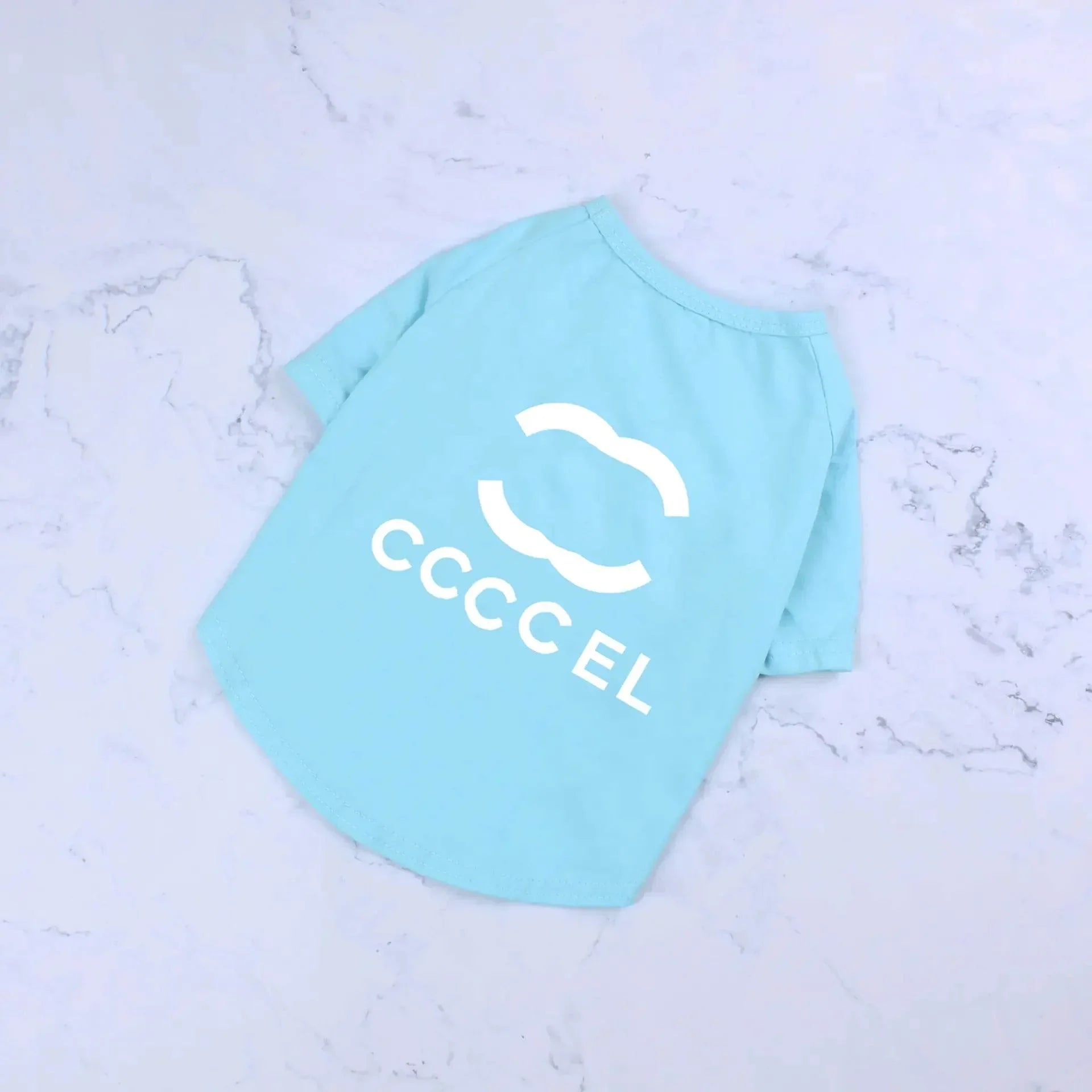 Light blue pet T-shirt with white logo, ideal for dogs or cats, displayed on marble background