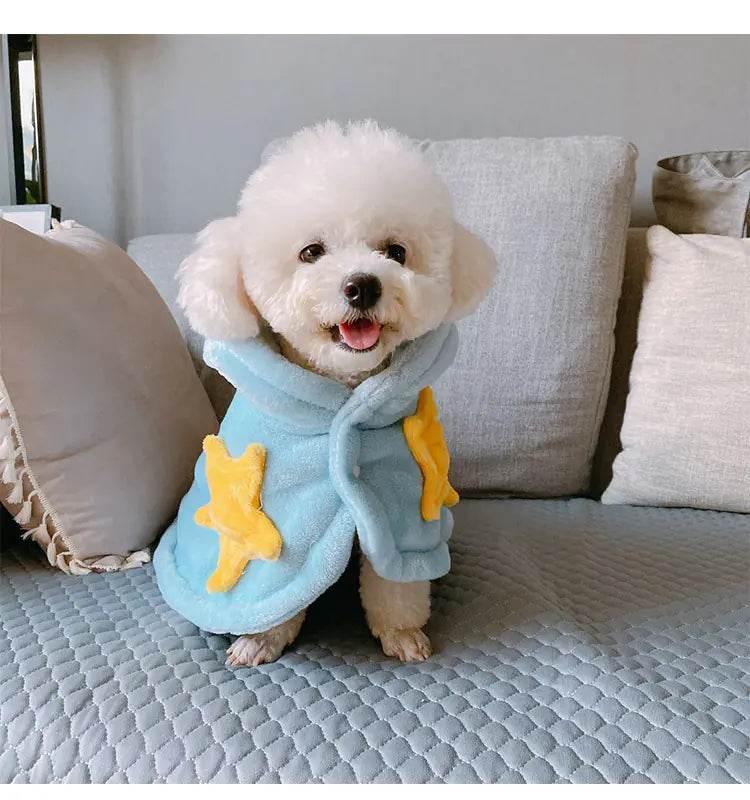 Fluffy white dog wearing cozy blue pet robe with yellow stars, sitting on sofa