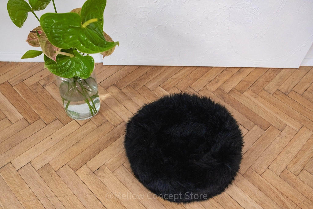 Black fluffy pet bed on wooden floor beside green plant, cozy pet accessory for dogs and cats