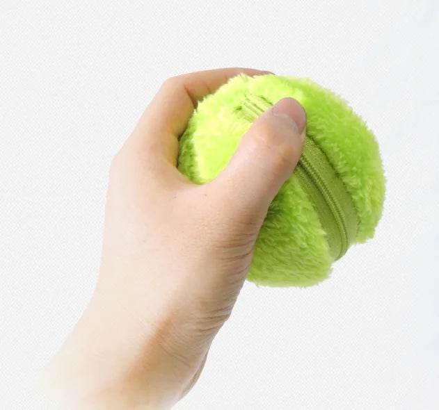 Hand squeezing bright green plush dog toy ball with zipper, pet play accessory