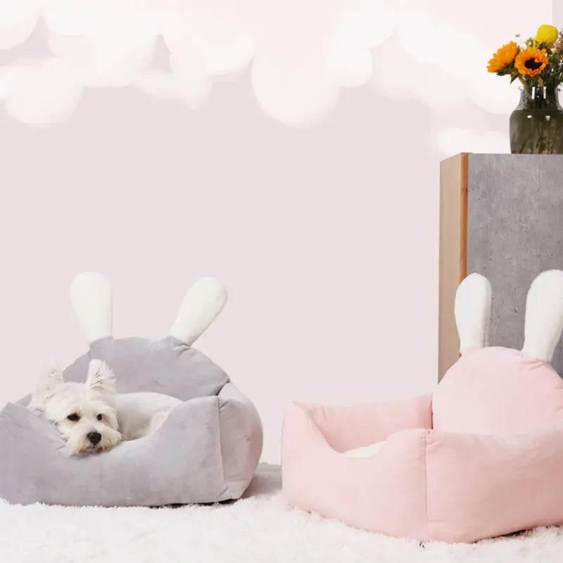 Cute white dog resting in gray bunny ear pet bed, pink version beside, cozy pet accessories
